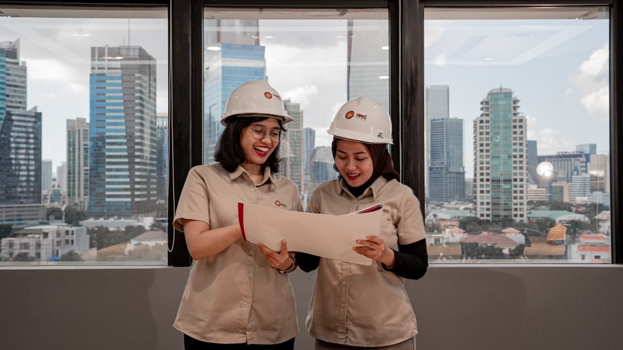 Two people in hard hats reviewing blueprints together indoors