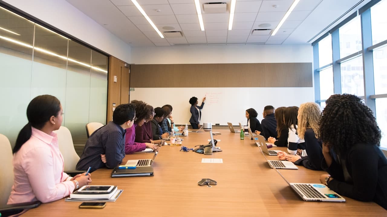 Colleagues around a conference table listening to a woman speaking
