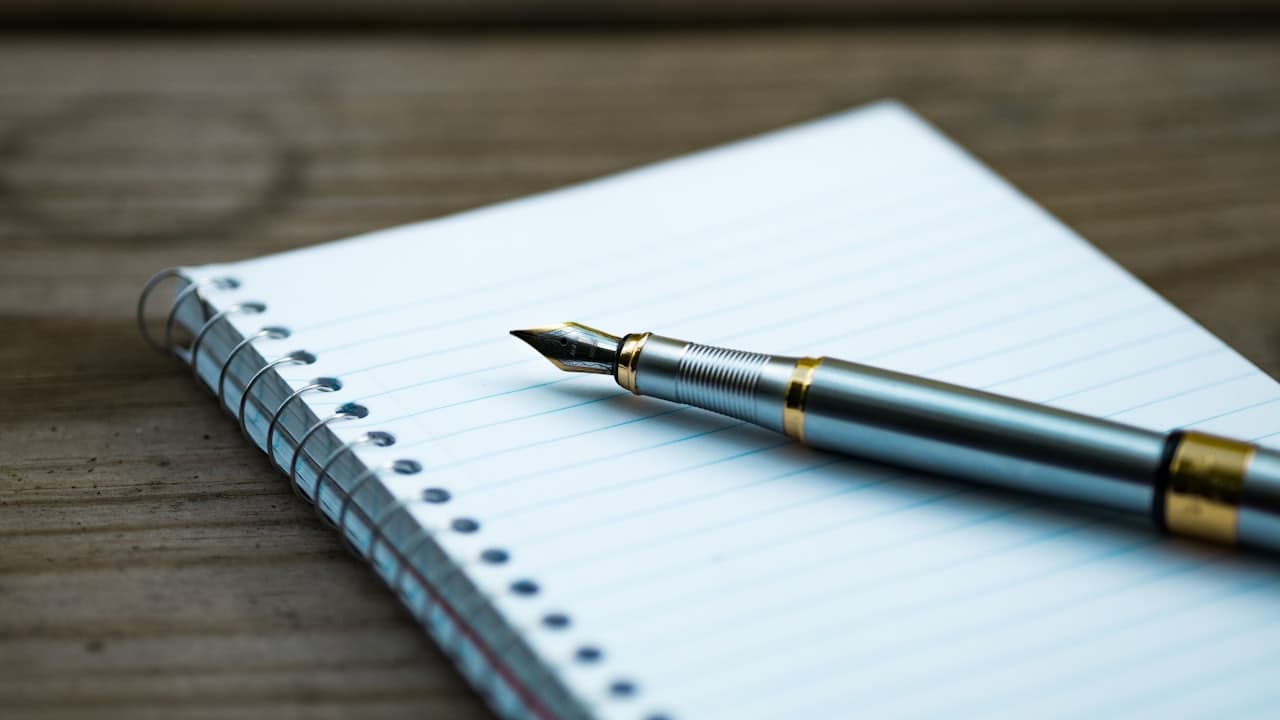 A fountain pen resting on an open spiral notebook
