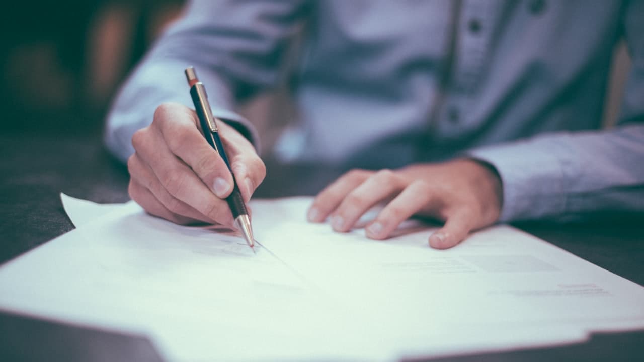 A person signing a contract with a pen at a desk