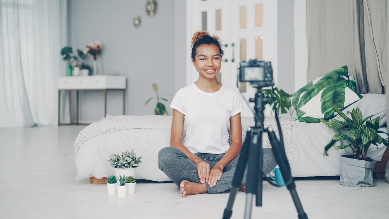 A young woman filming herself at home with a camera on a tripod