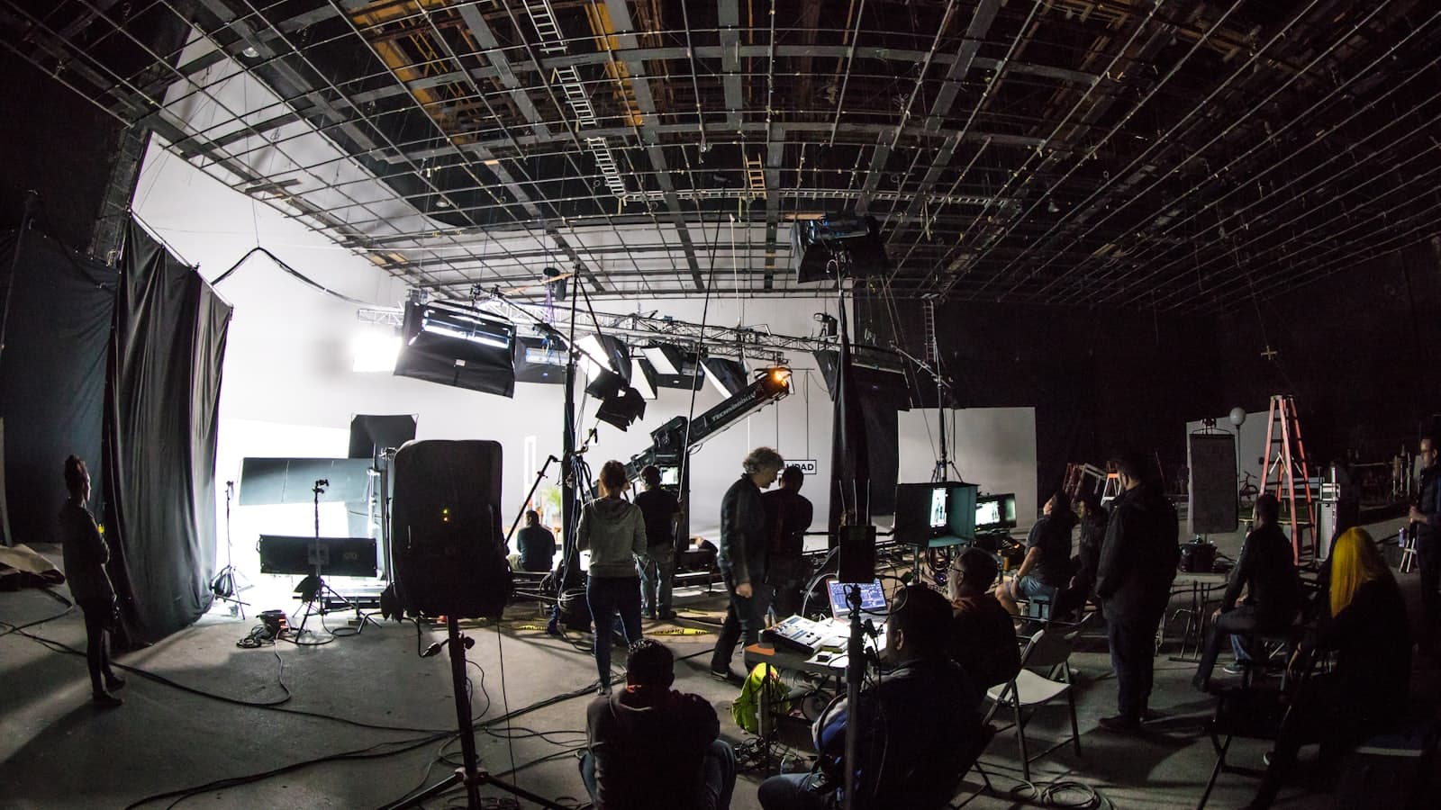 A film crew working on a lit soundstage with cameras and grip equipment